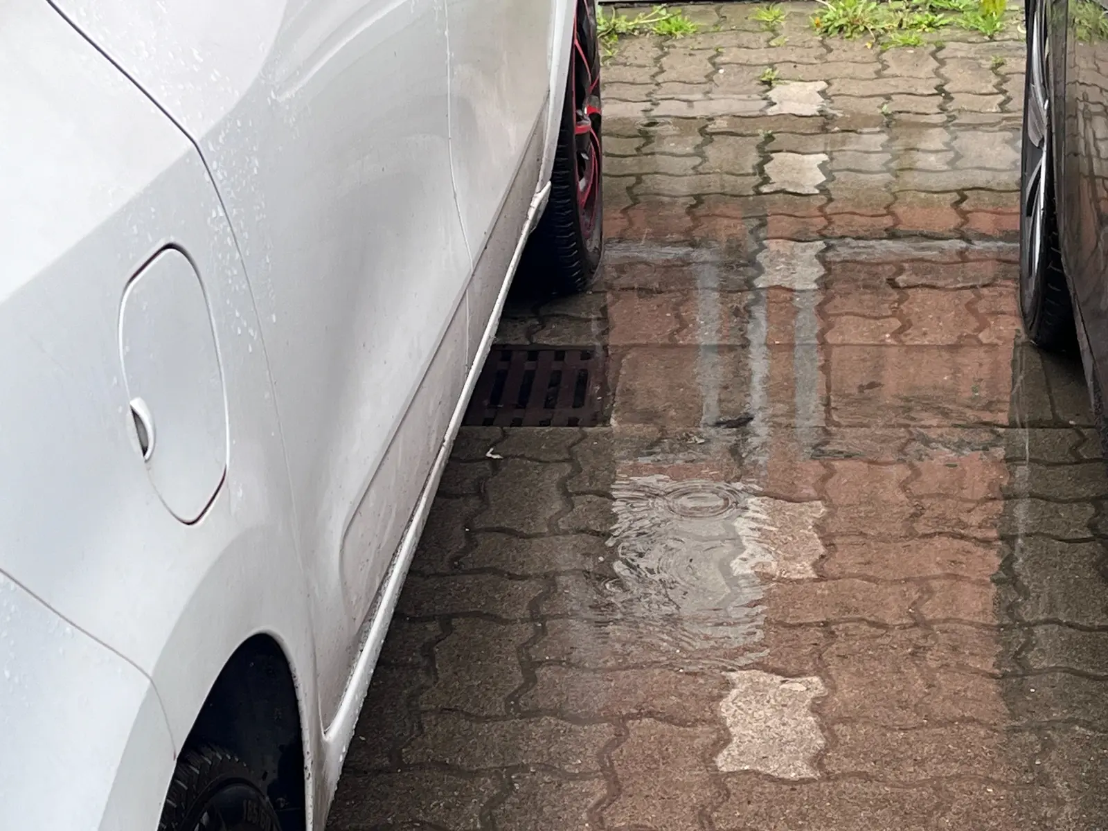 Wasser fließt bei Regen in einen Ablauf auf einer Parkfläche